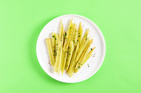 Braised celery on plate over green background with free text space. Top view, flat lay