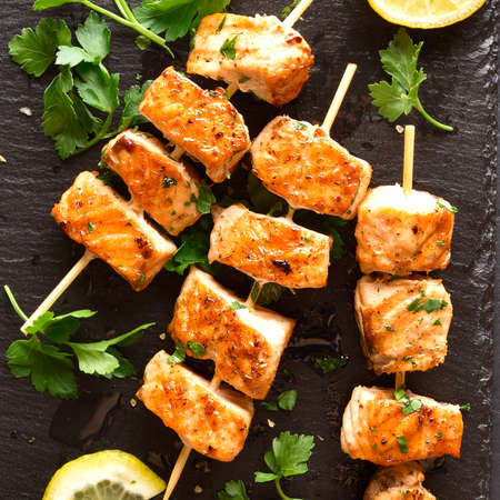 Close up view of grilled salmon kebab. Barbecue salmon skewers on black stone board. Top view, flat layの写真素材