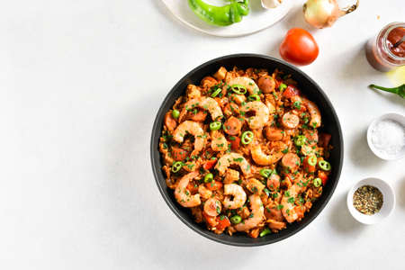 Creole jambalaya with chicken, smoked sausages and vegetables in frying pan on white stone background with copy space. Top view, flat lay, close upの写真素材
