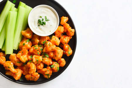 Vlose up view of cauliflower buffalo wings with celery and sauce on plate over white stone background with free text space. Healthy eating, plant based food concept. Top view, flat layの写真素材