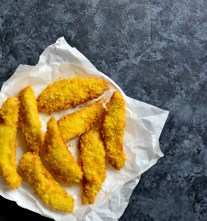 Crispy fried breaded chicken breast strips on paper over blue stone background. Top view, flat lay
