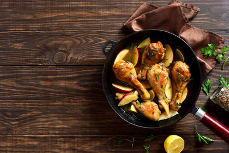 Chicken drumsticks baked with apples and herbs in frying pan on wooden background with free text space. Top view, flat layの写真素材