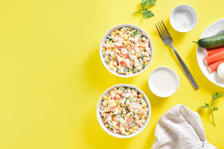 Imitation crab salad with crab sticks, corn, eggs, cucumber and rice in bowls over yellow background with copy space. Top view, flat layの写真素材