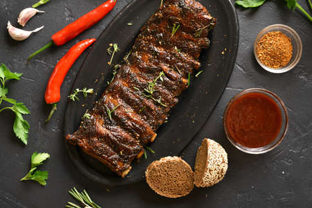Grilled spare ribs on plate over black stone background. Tasty bbq meat. Top view, flat layの写真素材