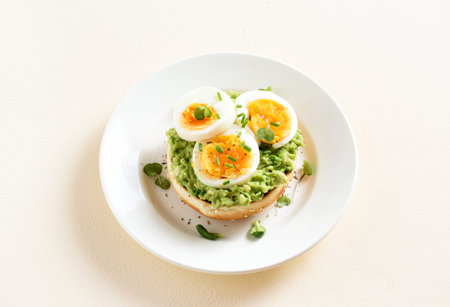 Avocado toast bun with eggs on plate over light stone background with free text space.