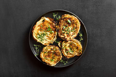 Baked cabbage steaks on plate over black stone background. Top view, flat layの写真素材