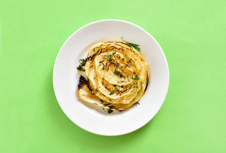 Roasted cabbage steak on plate over green background. Top view, flat layの写真素材