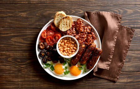 Full English breakfast with fried egg, bacon, sausage, beans and mushrooms on wooden background. Top view, flat layの写真素材