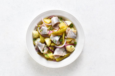 Herring salad with boiled potatoes, pickled cucumbers and red onion in bowl over light stone background with free text space. Top view, flat layの写真素材