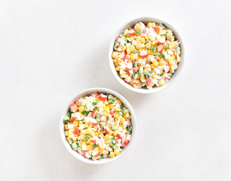 Russian style imitation crab salad with crab sticks, corn, eggs, cucumber and rice over white...