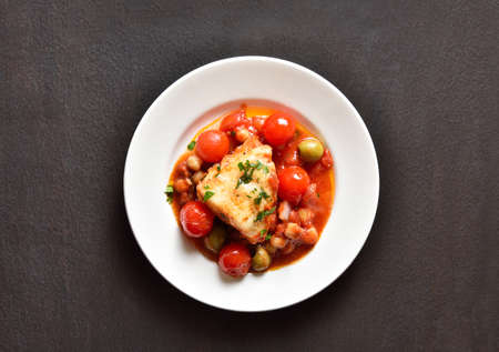 Cod stew with chickpeas, cherry tomatoes and olives on plate over dark stone background. Top view, flat layの写真素材