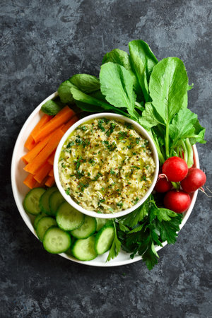 Baba ganoush (roasted eggplant dip) and fresh organic vegetables over plate ove dark stone background. Healthy eating. Top view, flat layの写真素材