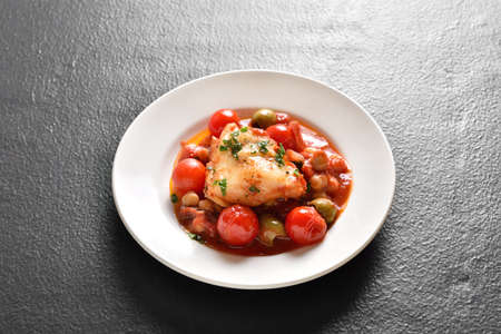 Cod stew with chickpeas, cherry tomatoes and olives on plate over dark stone background. Close up viewの写真素材