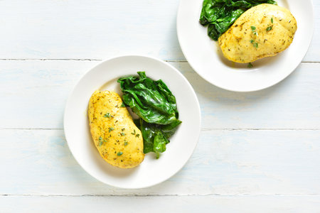 Delicious baked turmeric chicken breast with sauteed spinach on plate over light wooden background with free text space. top view, flat layの写真素材
