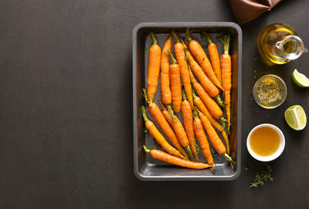 Roasted honey glazed carrots on baking tray over dark stone background with free text space. Top view, flat layの写真素材