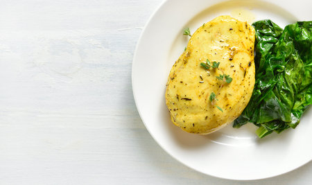 Close up view of baked turmeric chicken breast and sauteed spinach on plate over light wooden background with free text space. Top view, flat layの写真素材