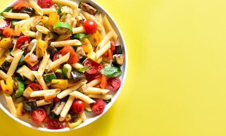 Close up view of penne pasta salad with roasted vegetables on plate over yellow background with free text space. Top view, flat layの写真素材