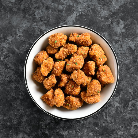 Crispy fried breaded chicken bites in bowl over dark stone background. Top view, flat layの写真素材