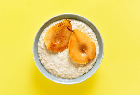 Oat porridge with caramelized pear in bowl over yellow background. top view, flat layの写真素材