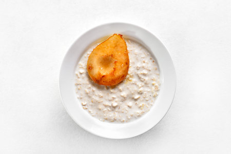 Oat porridge with caramelized pear in bowl over white background. Top view, flat layの写真素材