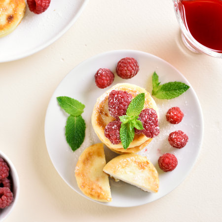Cottage cheese pancakes with fresh raspberries on plate over light stone background. top view, flat layの写真素材