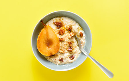 Oatmeal with caramelized pear and walnut in bowl over yellow background. top view, flat layの写真素材