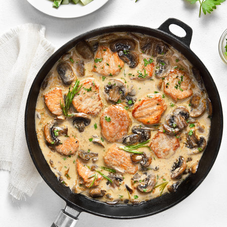 Close up view of pork medallions with mushroom sauce in cast iron pan over white stone background. top view, flat layの写真素材