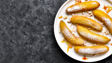 Deep fried bananas on white plate over dark stone background with free space. Top view, flat layの写真素材