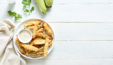 Baked crispy zucchini fries with dipping sauce on plate over light wooden background with free space. Top view, flat layの写真素材