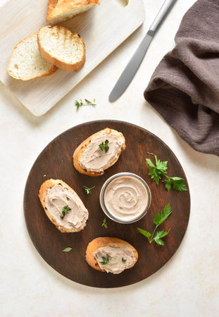 Chicken liver pate on toasted bread on wooden cutting board over light background. Top view, flat...