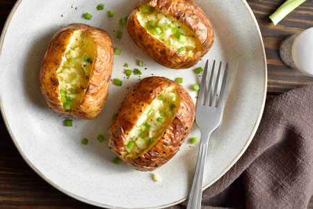 Close up view of oven baked potato with green onion on white plate over wooden table. Top view, flat layの写真素材