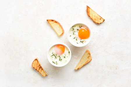 Eggs en cocotte (baked eggs) in ramekins with cream, cheese and greens and slices toasted bread over...