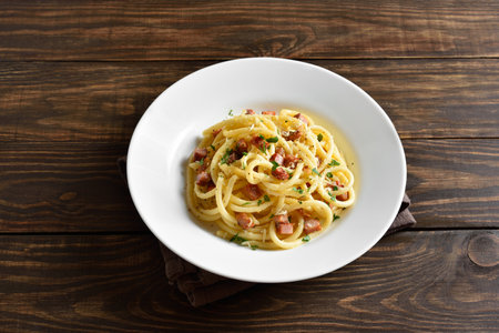 Carbonara pasta, spaghetti with crisp pancetta bacon and black pepper on white plate on wooden table. Traditional Italian cuisine. Country style, close up viewの写真素材