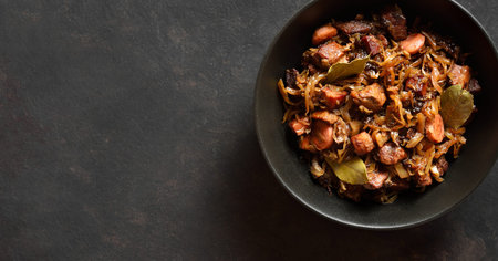 Traditional polish Bigos in bowl over dark stone background with copy space. Stewed cabbage with...