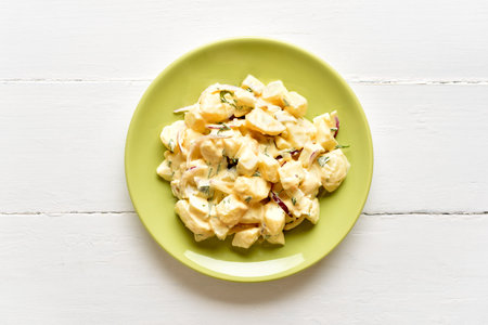 Homemade potato salad with egg, pickle, onion with mayonnaise and yogurt dressing on green plate on white wooden background. Top view, flat layの写真素材