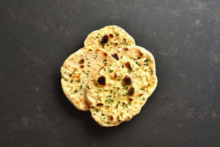 Indian naan bread with greens on dark stone background. Top view, flat lay