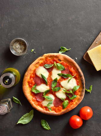 Pizza with mozzarella, pepperoni, tomato sauce and basil. Homemade pizza with tomatoes, cheese, sausage on dark background with free space. Top view, flat lay.の写真素材