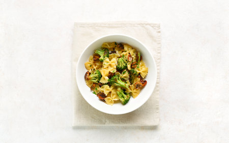 Farfalle pasta with roasted broccoli and mushrooms in bowl on white background with copy space. Homemade prepared dish of farfalle pasta with roasted broccoli and sautÃ©ed mushrooms. Top view, flat layの写真素材