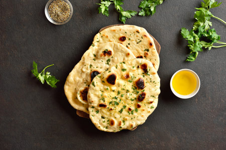 Indian naan bread with greens and garlic butter on dark brown stone background. Top view, flat lay