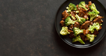 Thinly sliced beef meat with roasted broccoli. Beef with broccoli on plate over dark stone background with copy space. Top view, flat layの写真素材