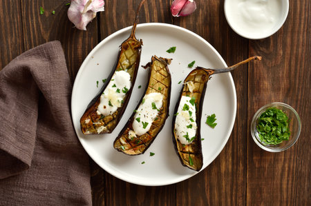Baked aubergine with garlic yoghurt dressing on white plate over wooden background. Top view, flat layの写真素材