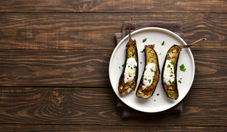 Baked aubergine with garlic yoghurt dressing on plate over wooden background with free space. Top view, flat layの写真素材