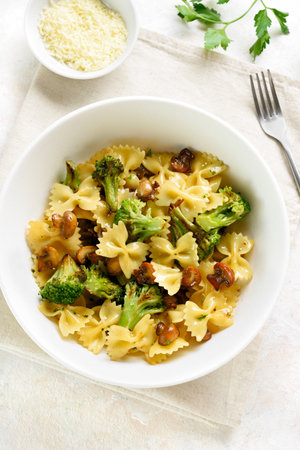 Farfalle pasta with roasted broccoli and mushrooms on light background. Homemade prepared dish of farfalle pasta with roasted broccoli and sautÃ©ed mushrooms served in white bowl. Top view, flat layの写真素材