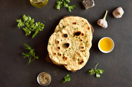 Indian naan bread with greens and garlic butter on dark stone background. Top view, flat layの写真素材