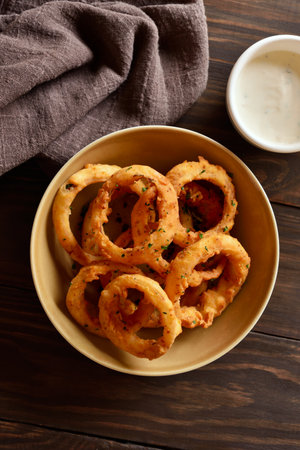Crispy fried onion rings in bowl on wooden table. Top view, flat layの写真素材