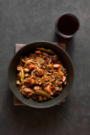 Traditional polish Bigos in bowl over dark stone background. Stewed cabbage with sauerkraut, mushrooms, smoked meats and spices. Top view, flat layの写真素材