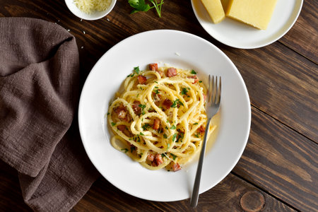 Carbonara pasta, spaghetti with crisp pancetta and black pepper on white plate on wooden background. Traditional Italian cuisine. Top view, flat layの写真素材