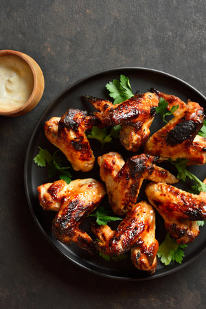 Bbq chicken wings on black plate over dark stone background. Top view, flat layの写真素材