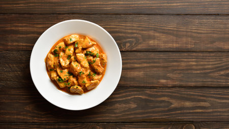 Traditional Indian dish chicken tikka masala. Butter chicken meat on white plate on brown wooden background with free text space. Top view, flat lay.の写真素材