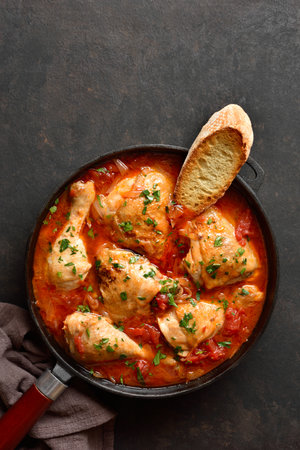 Delicious Georgian chicken stew with tomatoes and herbs (chakhokhbili) in cast iron skillet over dark stone background with copy space. Baked chicken with tomato gravy. Top view, flat layの写真素材